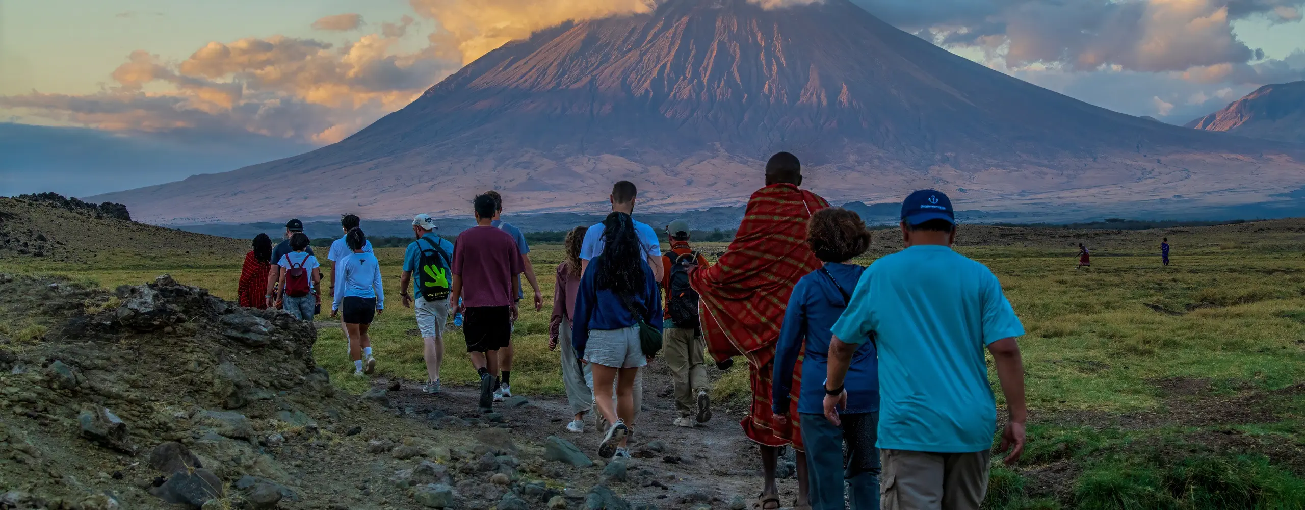 Travelers on a guided walk with a Maasai guide toward Ol Doinyo Lengai at sunset